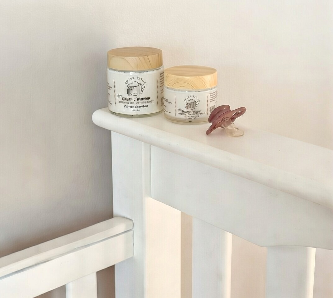Two jars of 100% organic Tallow Revive Body Butter and a pacifier on a white baby crib for babies.